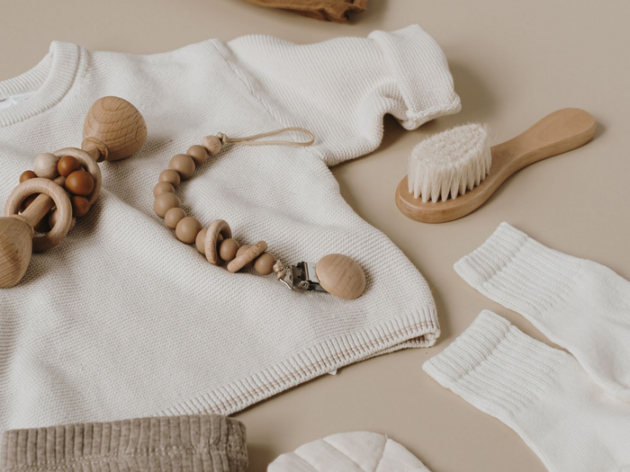 Des vêtements de bébé en tricot blanc et des jouets en bois disposés sur un fond beige