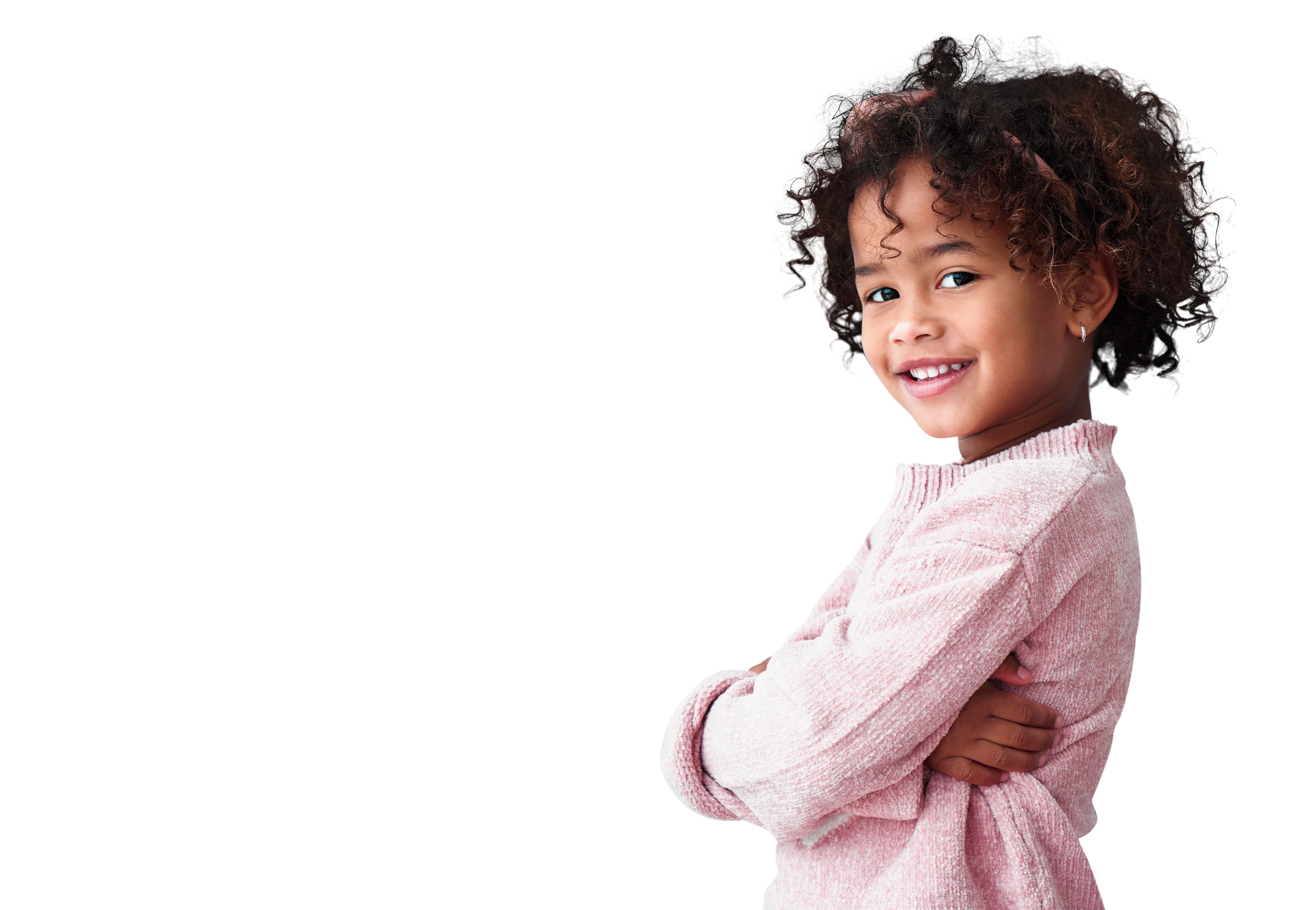 Enfant souriant aux cheveux bouclés, vêtu d'un pull rose, debout les bras croisés sur fond blanc