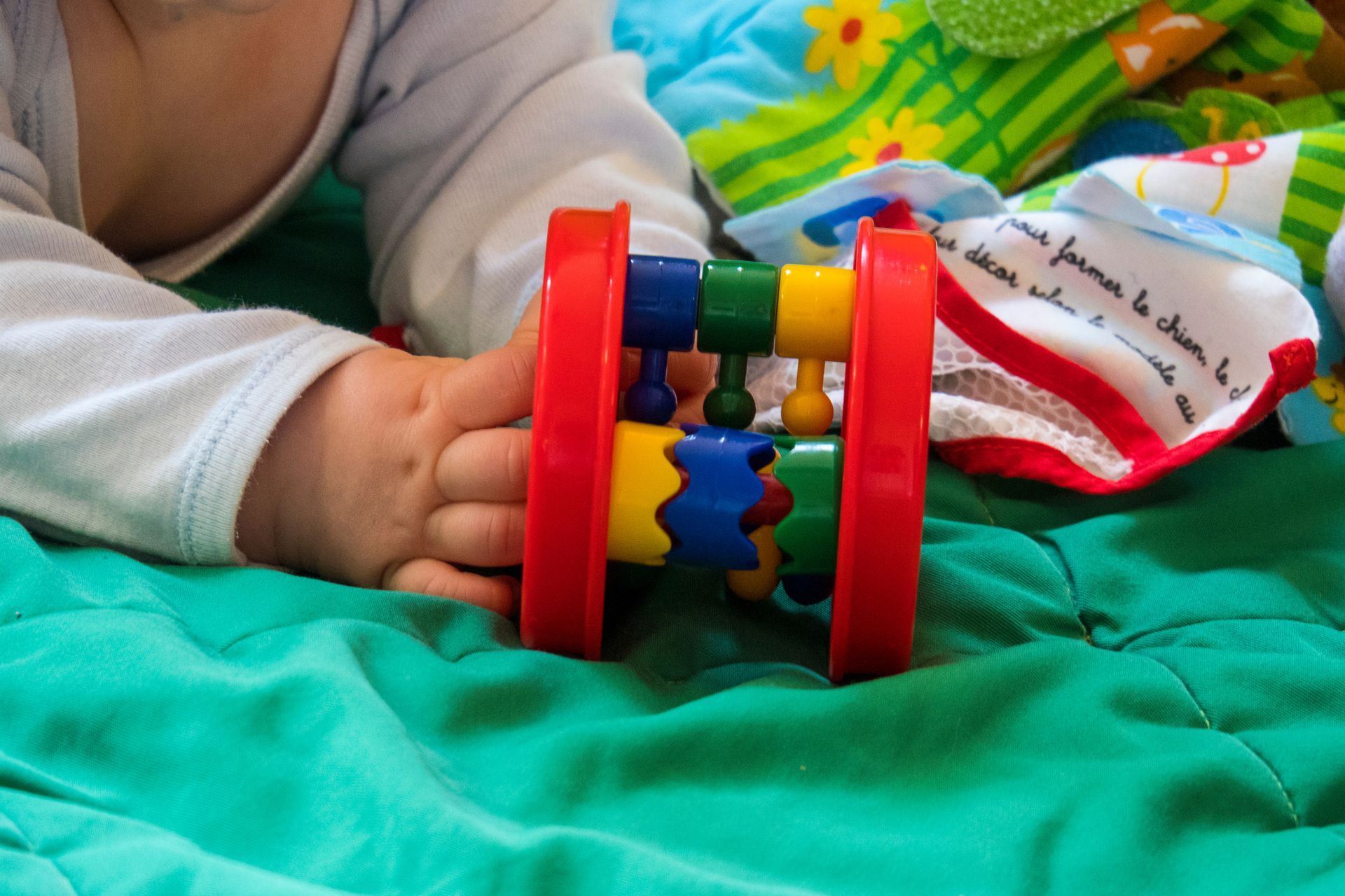 Bébé tenant un hochet coloré allongé sur une couette verte