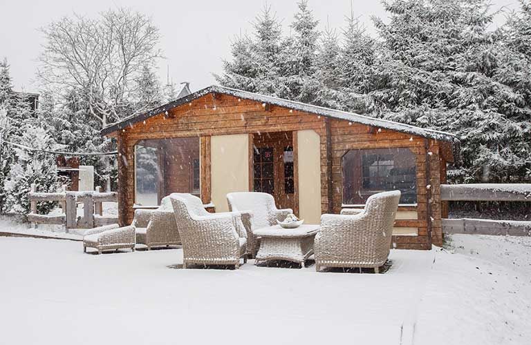 Ein schneebedecktes Holzhaus mit Korbmöbeln davor.