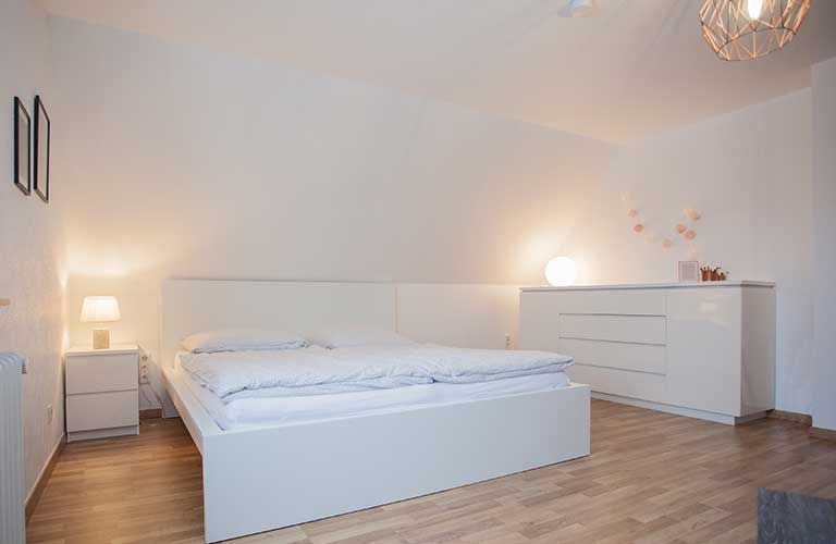 Ein Schlafzimmer mit Bett, Kommode, Nachttisch und Lampe.