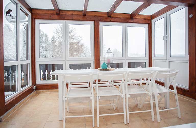 In dem Zimmer mit vielen Fenstern gibt es einen Tisch und Stühle.