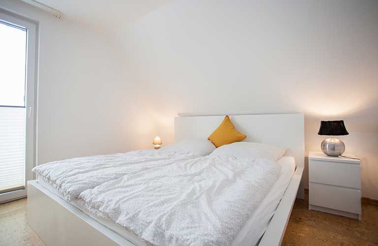 Ein Schlafzimmer mit Bett, Nachttisch, Lampe und Fenster.