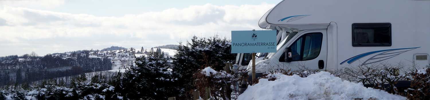 Ein weißes Wohnmobil steht im Schnee auf einem schneebedeckten Hügel.