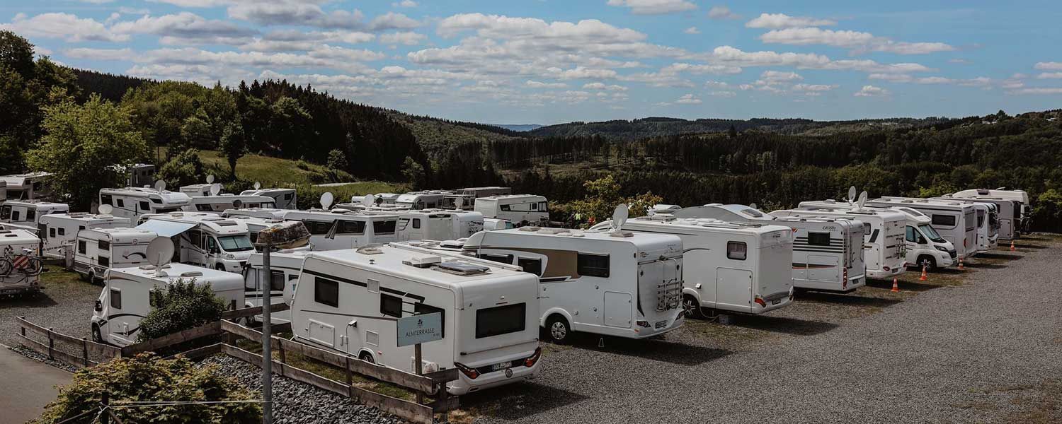 Eine große Gruppe Wohnmobile ist auf einem Schotterplatz geparkt.