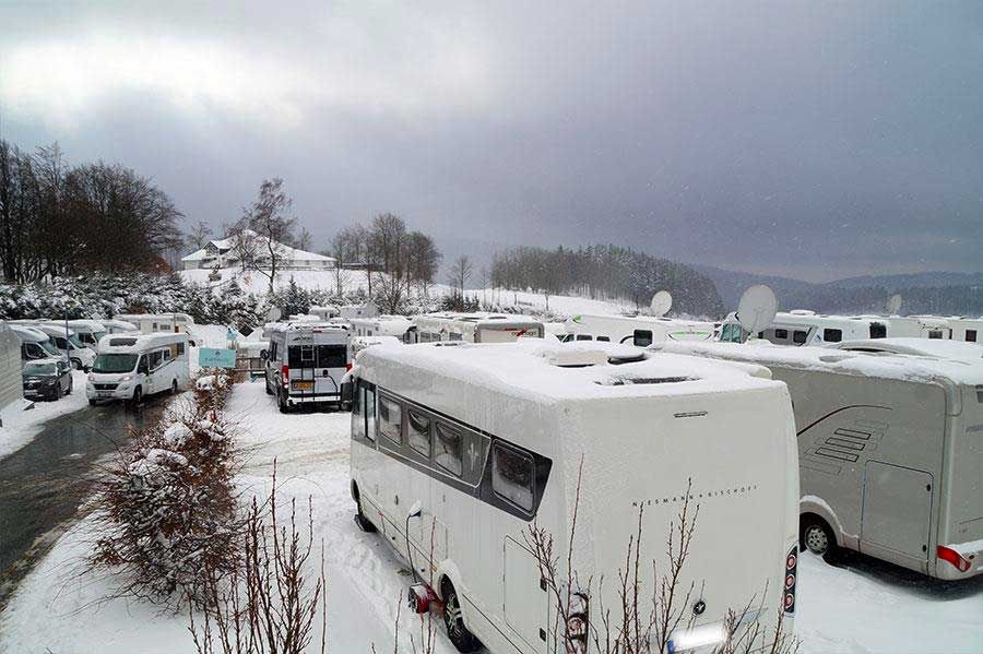 Viele wohnmobile stehen im schnee auf einem parkplatz.
