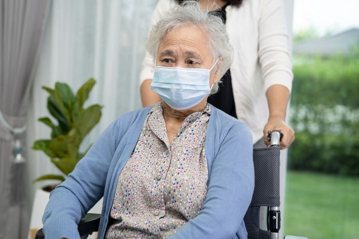 Una mujer mayor que lleva una máscara está sentada en una silla de ruedas.