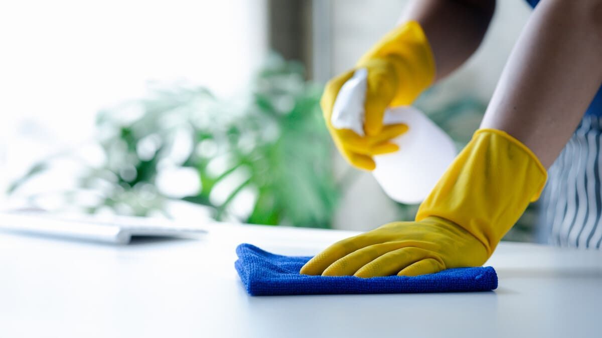 Una persona que lleva guantes amarillos está limpiando una mesa con un paño y una botella de spray.