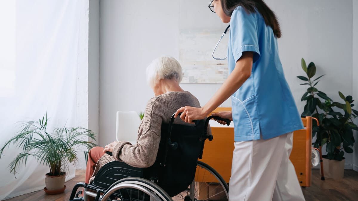 Una enfermera está ayudando a una mujer mayor en silla de ruedas.