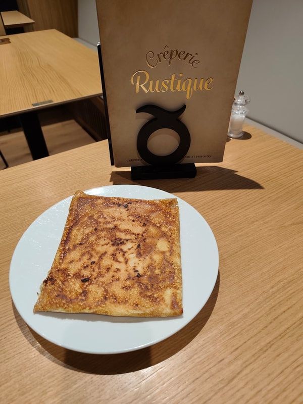 Crêpe sur une assiette blanche posée sur une table en bois, menu en arrière-plan.
