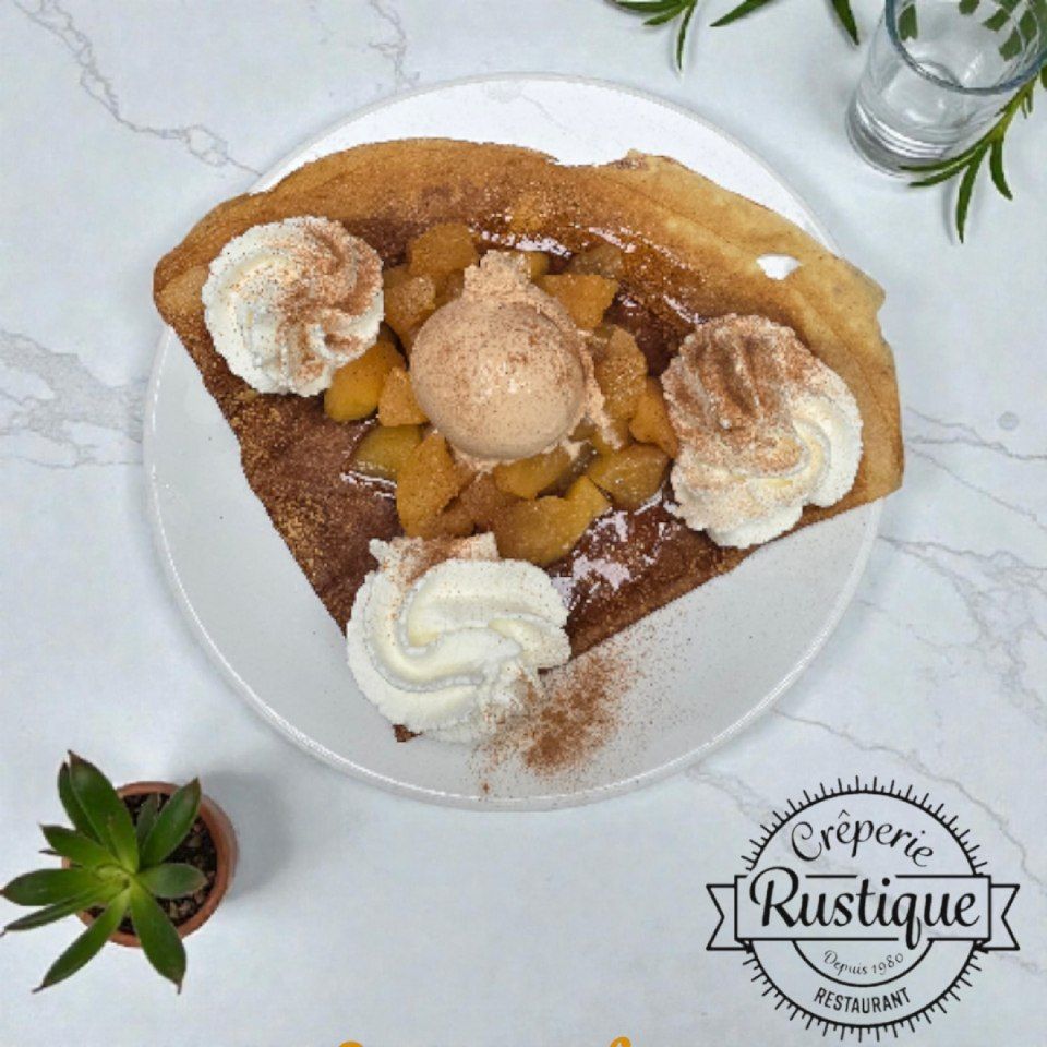 Crêpe aux pommes cuites, glace, crème fouettée et cannelle sur une assiette, étiquetée « Crêperie Rustique ».