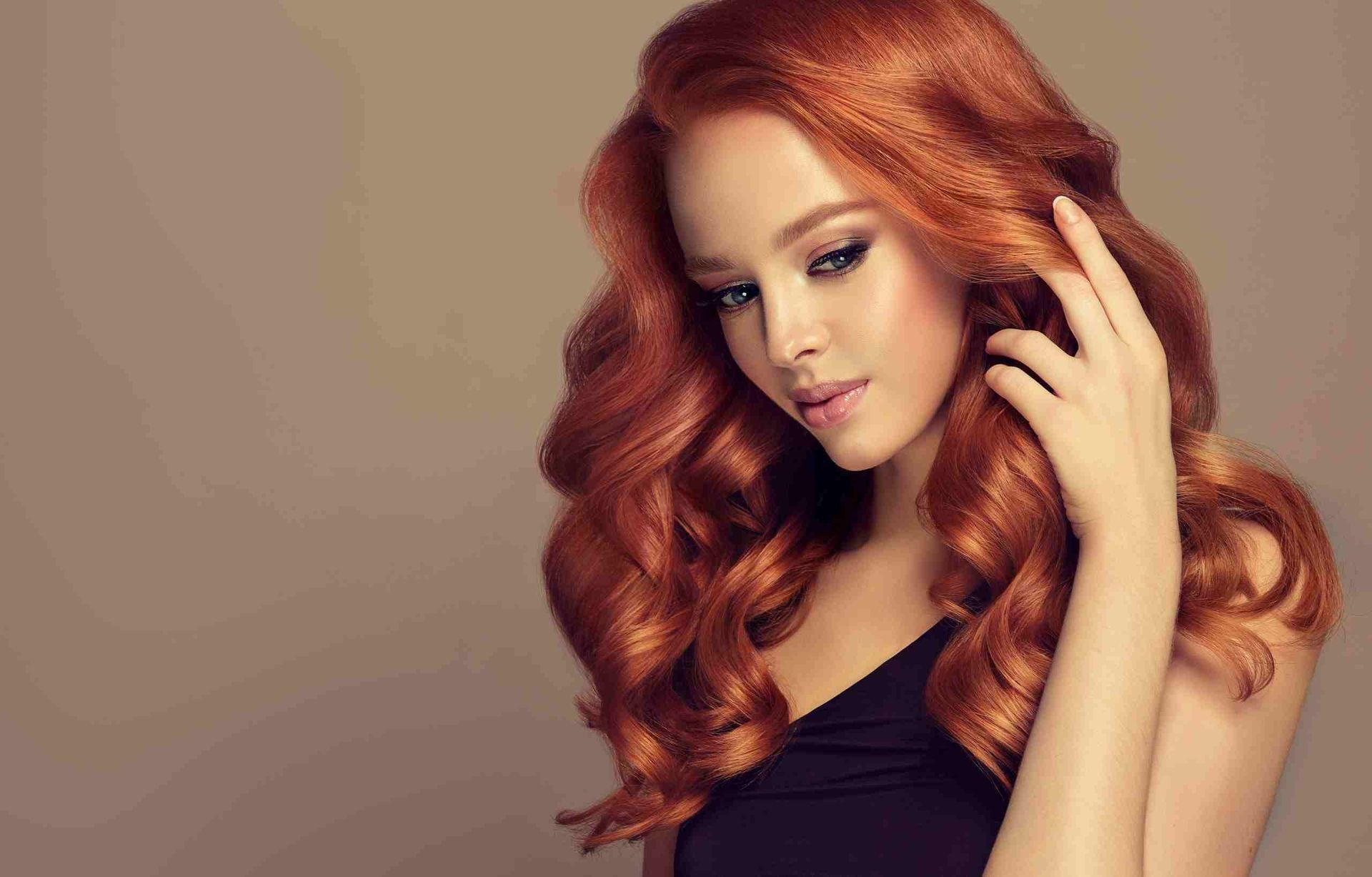 Una mujer con cabello largo y rojo lleva un vestido negro y se toca el cabello.