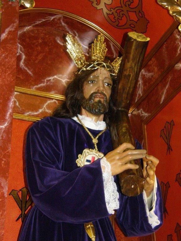 Una estatua de Jesús con una túnica púrpura sosteniendo una cruz de madera