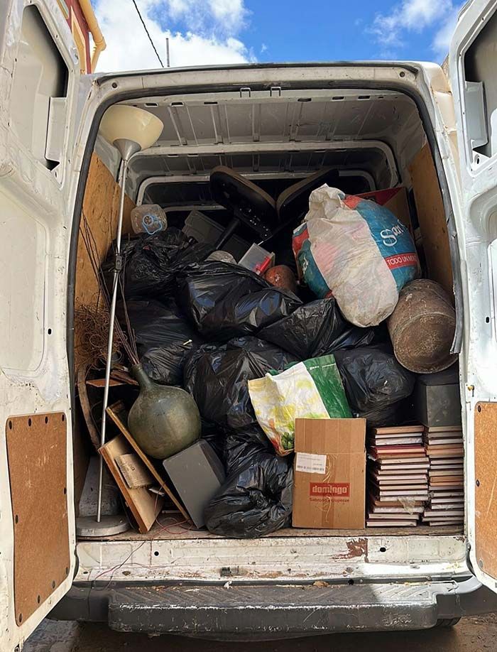 Parte trasera de una camioneta blanca llena de bolsas de basura, cajas y artículos diversos.