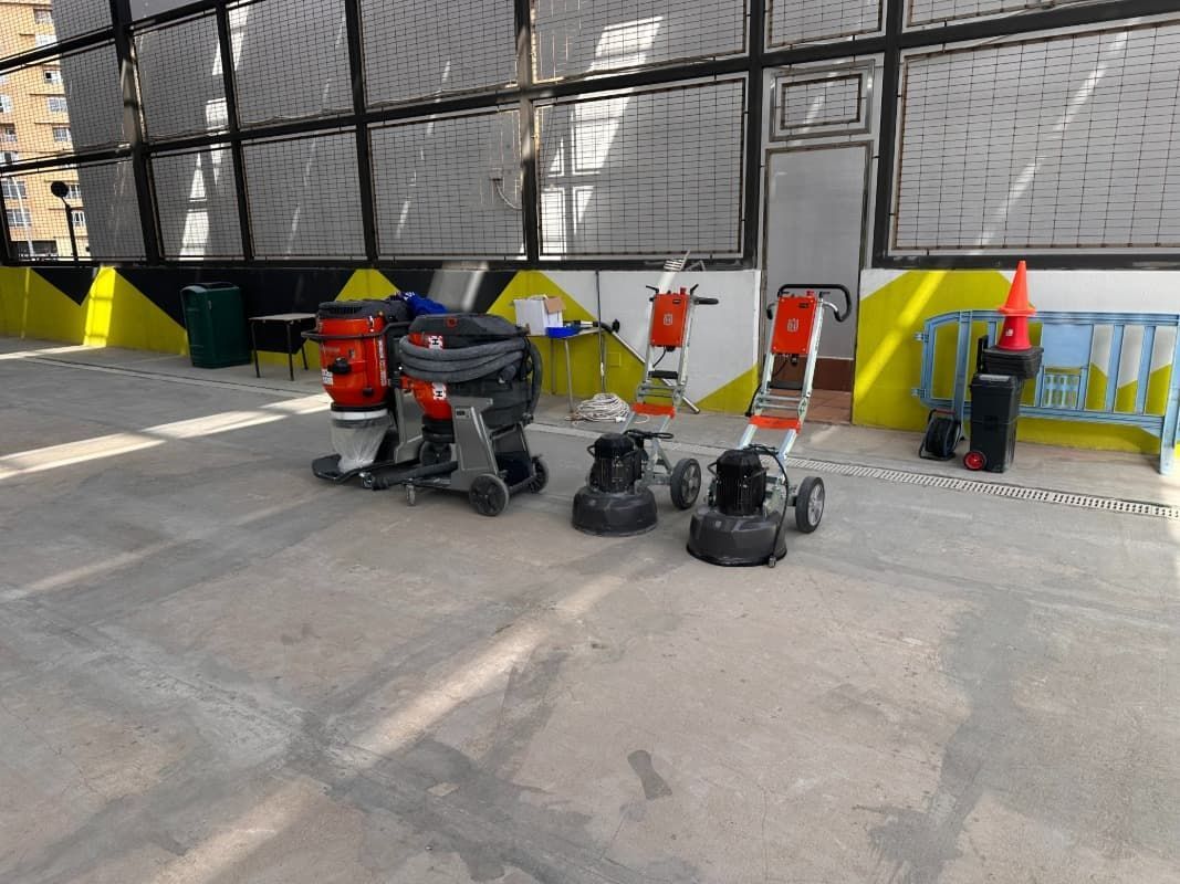 Diversas máquinas y herramientas industriales dispuestas sobre un suelo de hormigón cerca de una pared amarilla y negra.