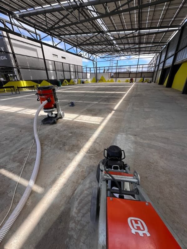 Almacén interior con suelo de hormigón, dos máquinas pulidoras y abundante luz natural que entra por la estructura abierta.