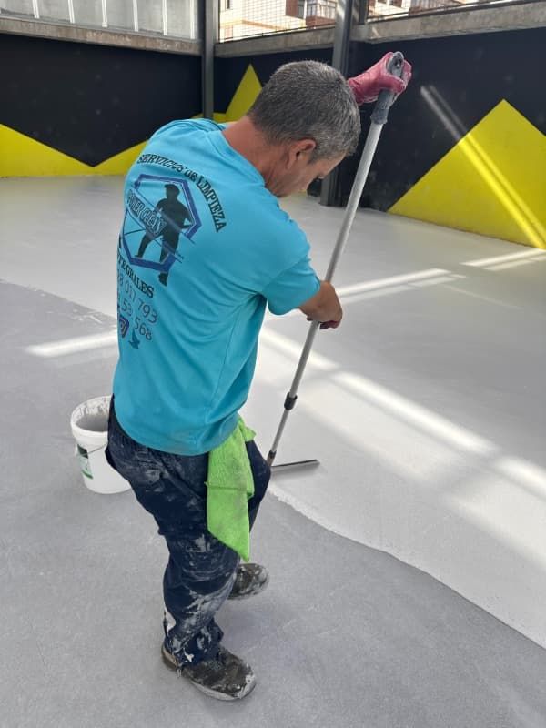 Trabajador pintando un suelo con un rodillo en un espacio industrial gris y amarillo.