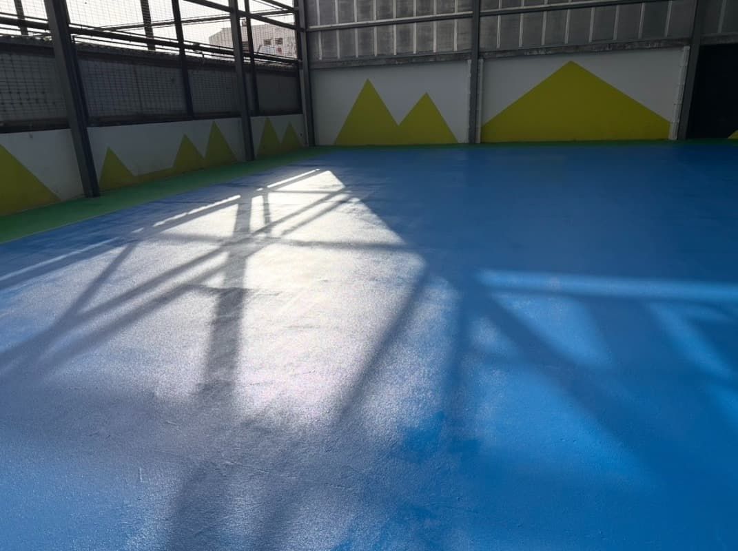 Pista deportiva cubierta azul con sombras iluminadas por el sol y detalles en las paredes de color amarillo.