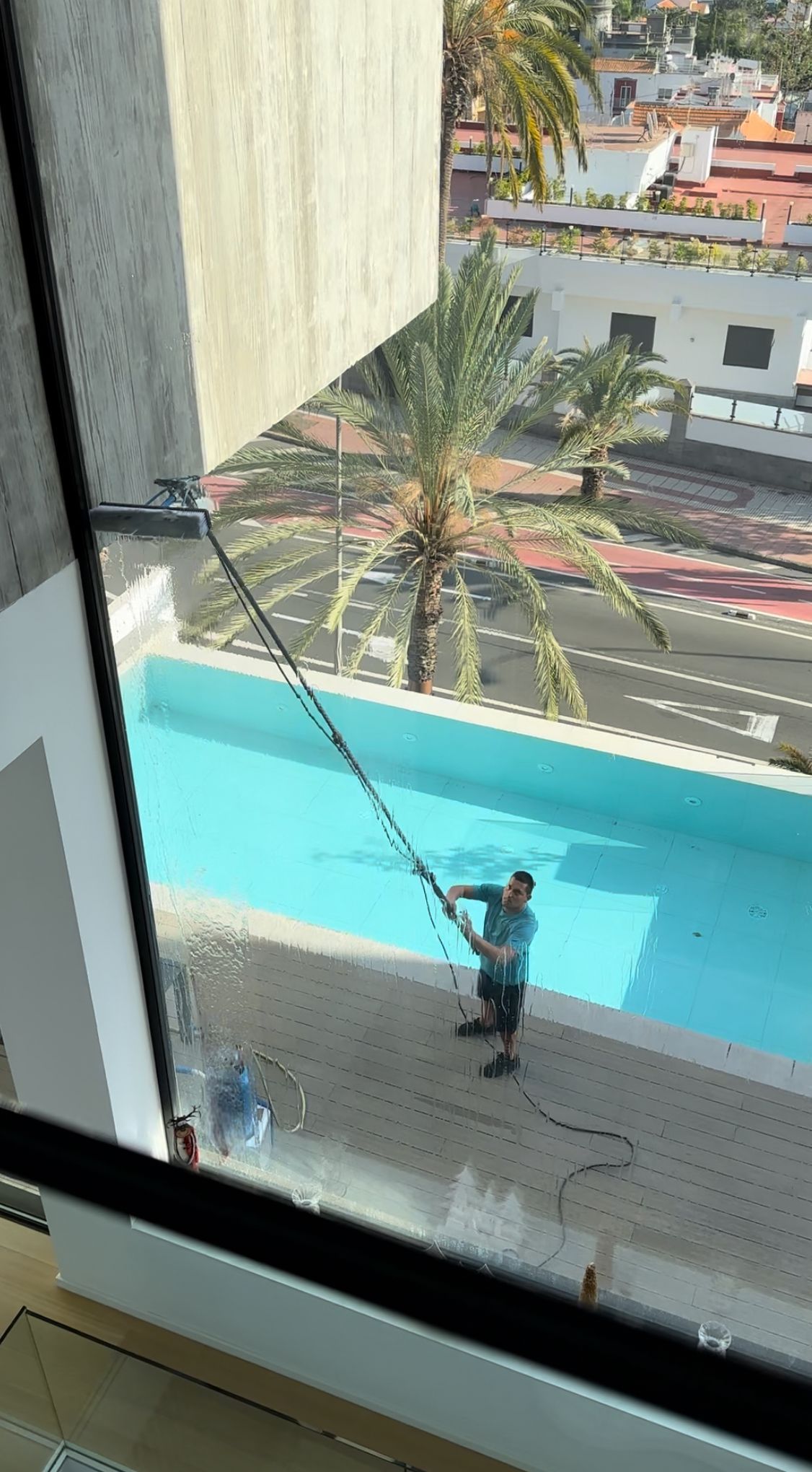 Un hombre está limpiando una ventana que da a una piscina.