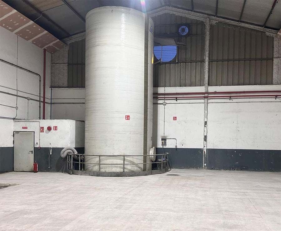 Gran tanque industrial de color blanco en un almacén, rodeado por una barandilla metálica.