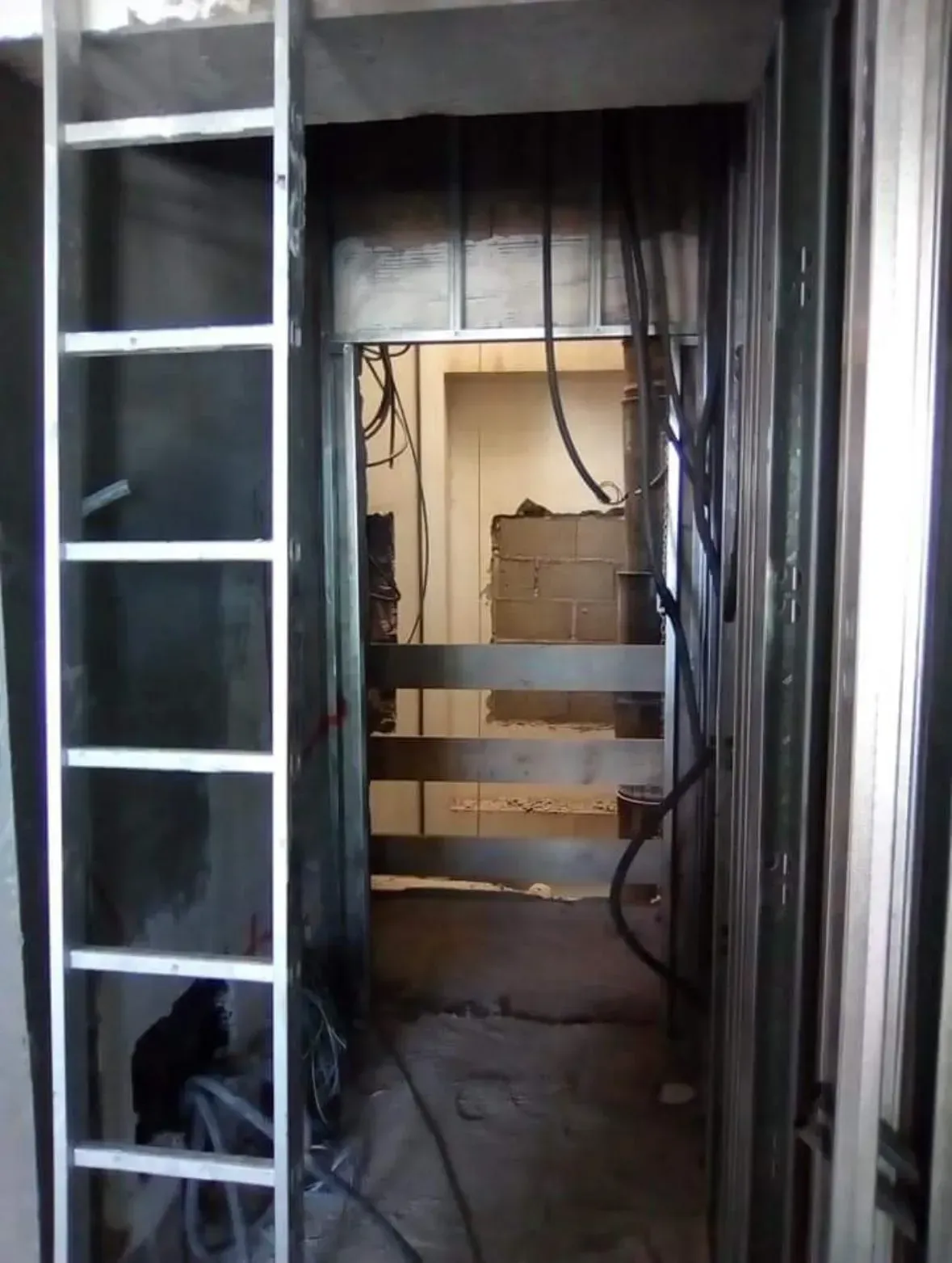 Sitio de construcción con una escalera a la izquierda, una puerta sin terminar y cables expuestos.