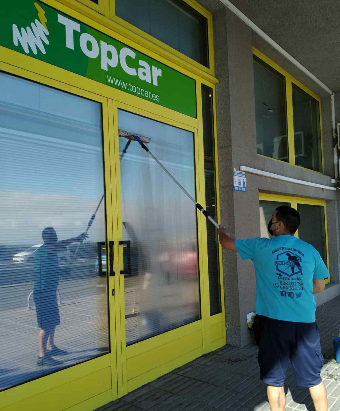 Un hombre está limpiando las ventanas de una importante tienda de automóviles.