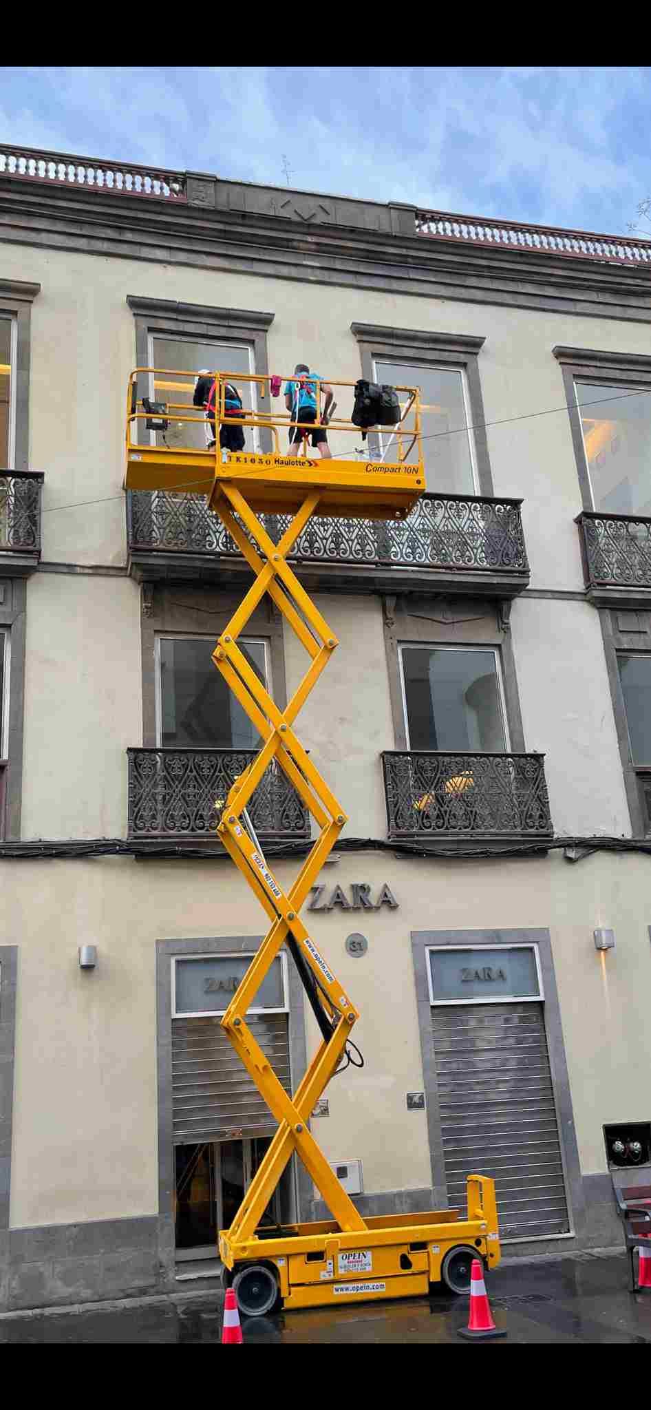 Se utiliza un elevador de tijera amarillo para limpiar las ventanas de un edificio.