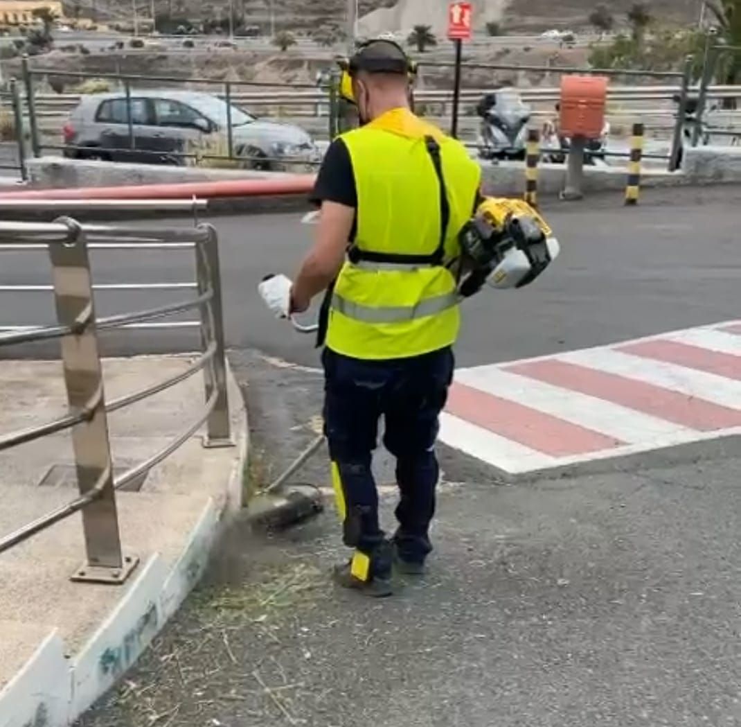 Un hombre con un chaleco amarillo camina por la calle sosteniendo una cortadora de césped.