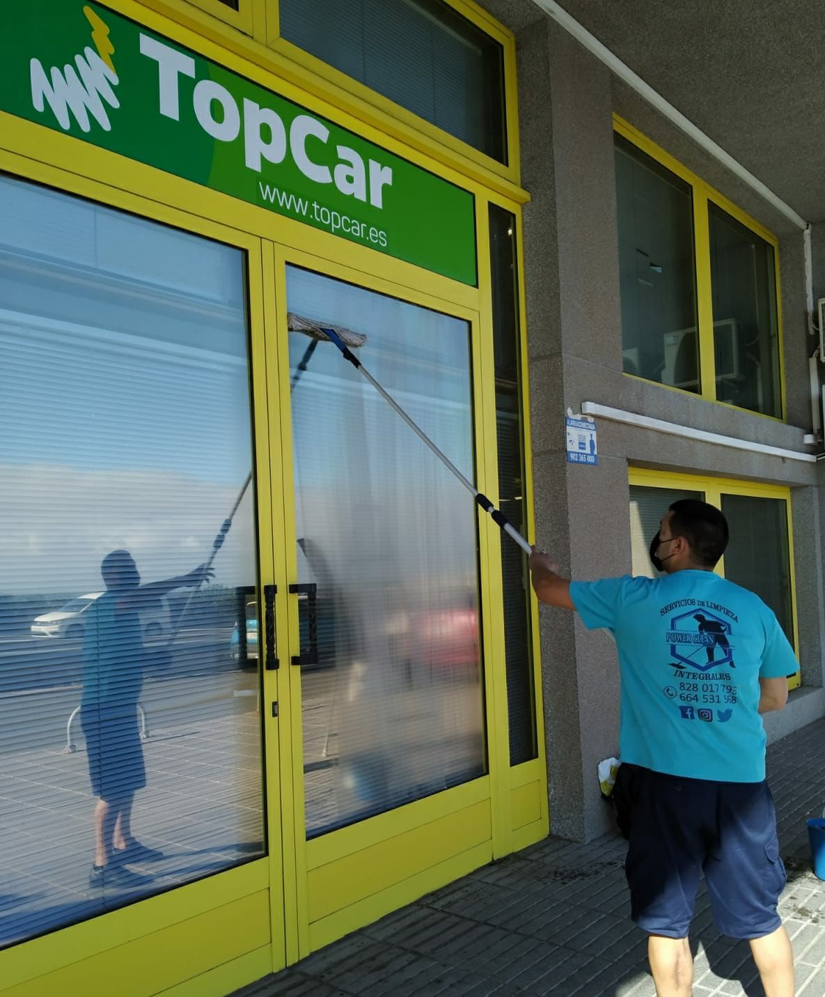 Un hombre está limpiando las ventanas de una importante tienda de automóviles.