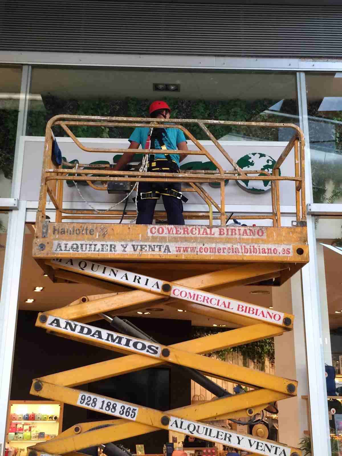Un hombre está parado en un elevador de tijera frente a un edificio.