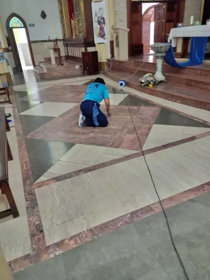 Persona arrodillada sobre un suelo estampado en el interior de una iglesia, limpiando.