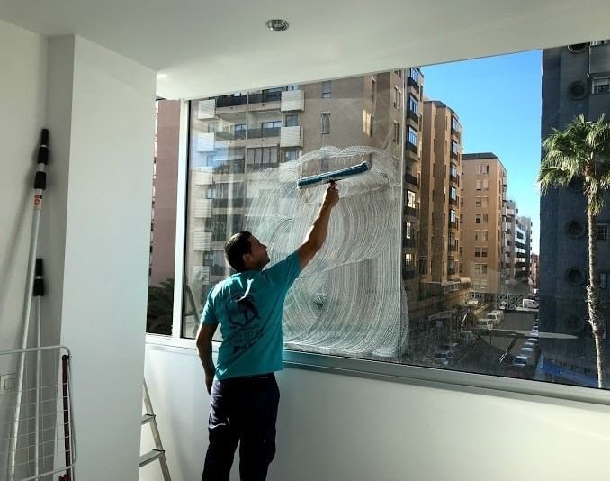 Un hombre está limpiando una ventana con una escobilla de goma.
