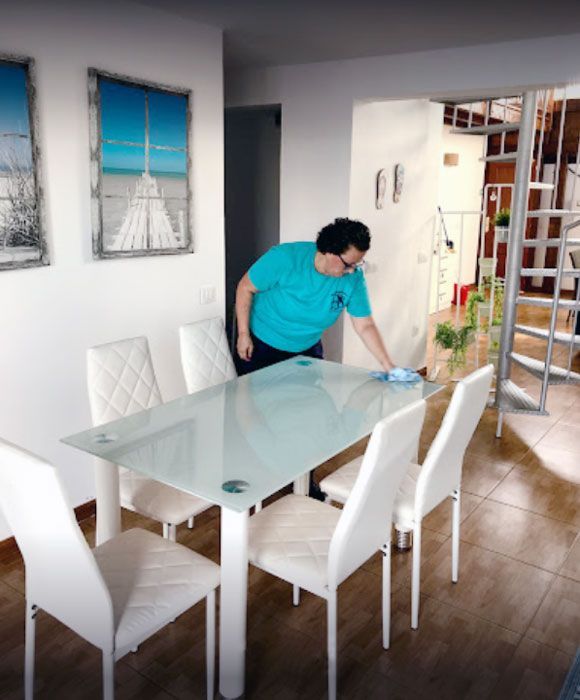 Un hombre con una camisa azul está limpiando una mesa de comedor de vidrio.