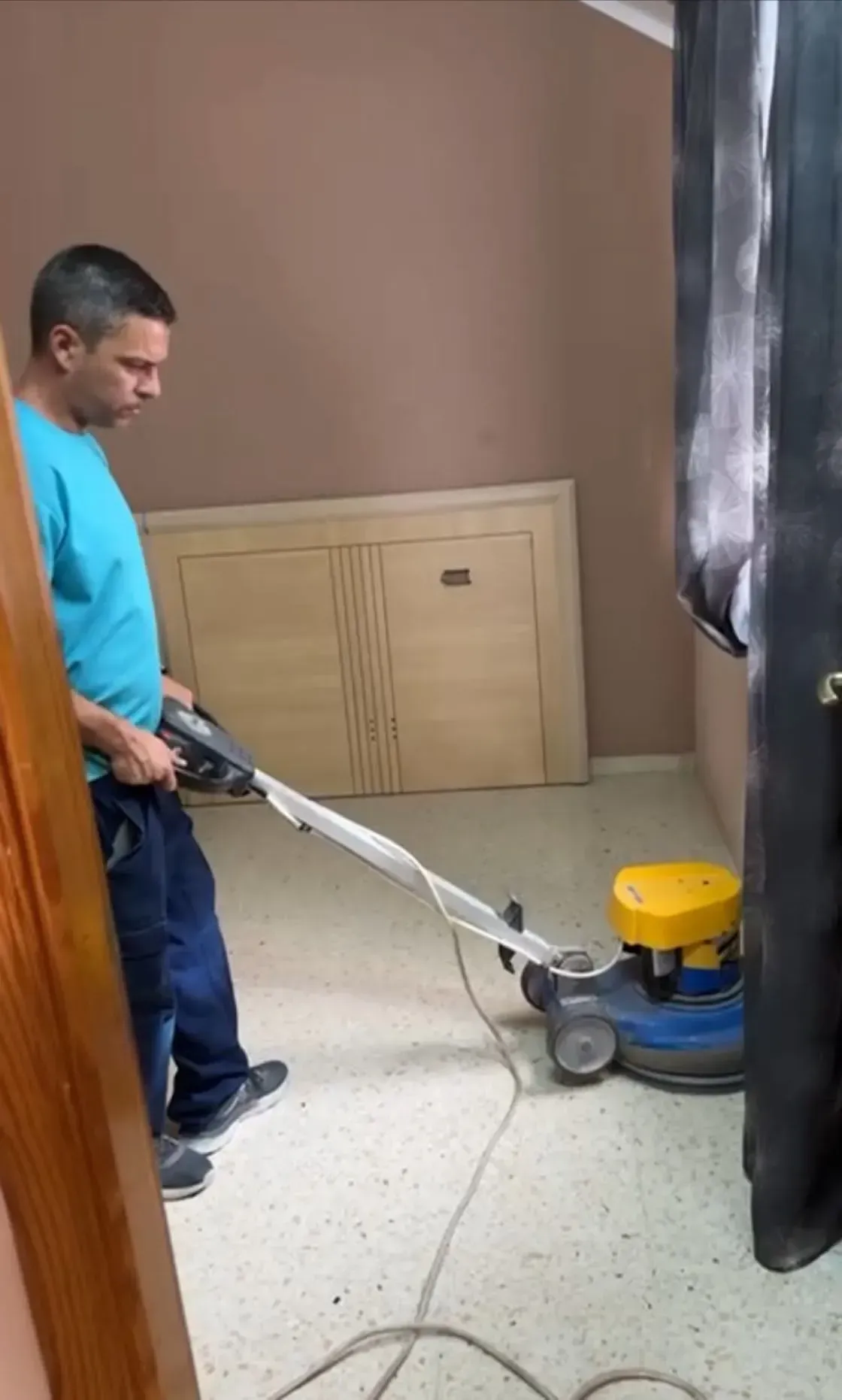 Hombre limpiando un suelo manchado con una pulidora en una habitación con la puerta cerrada.