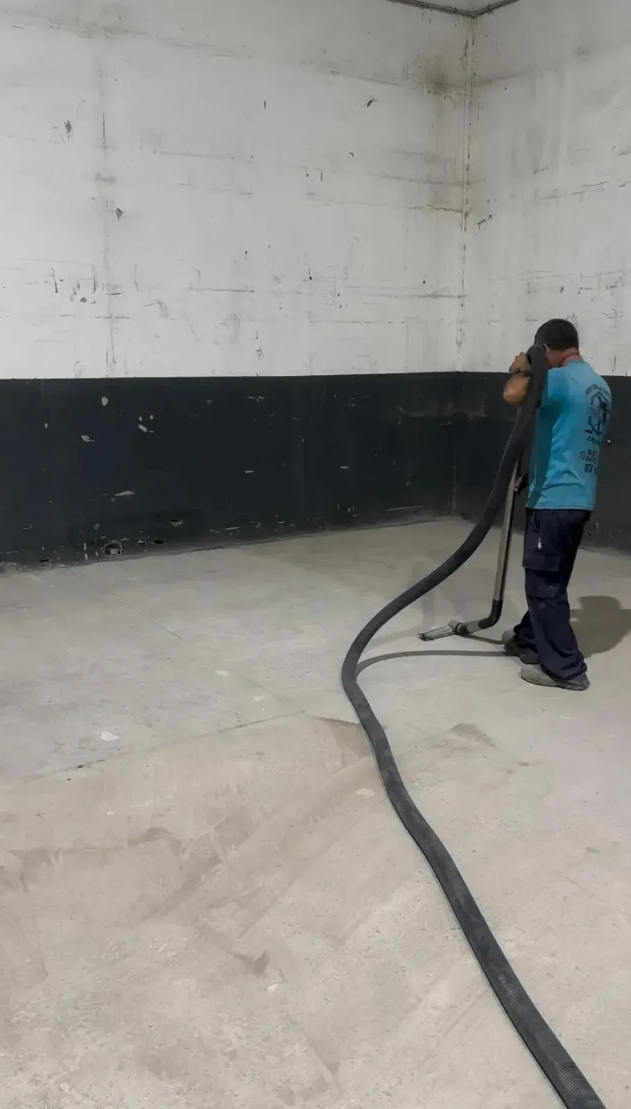 Un hombre está usando una aspiradora para limpiar un piso de concreto.