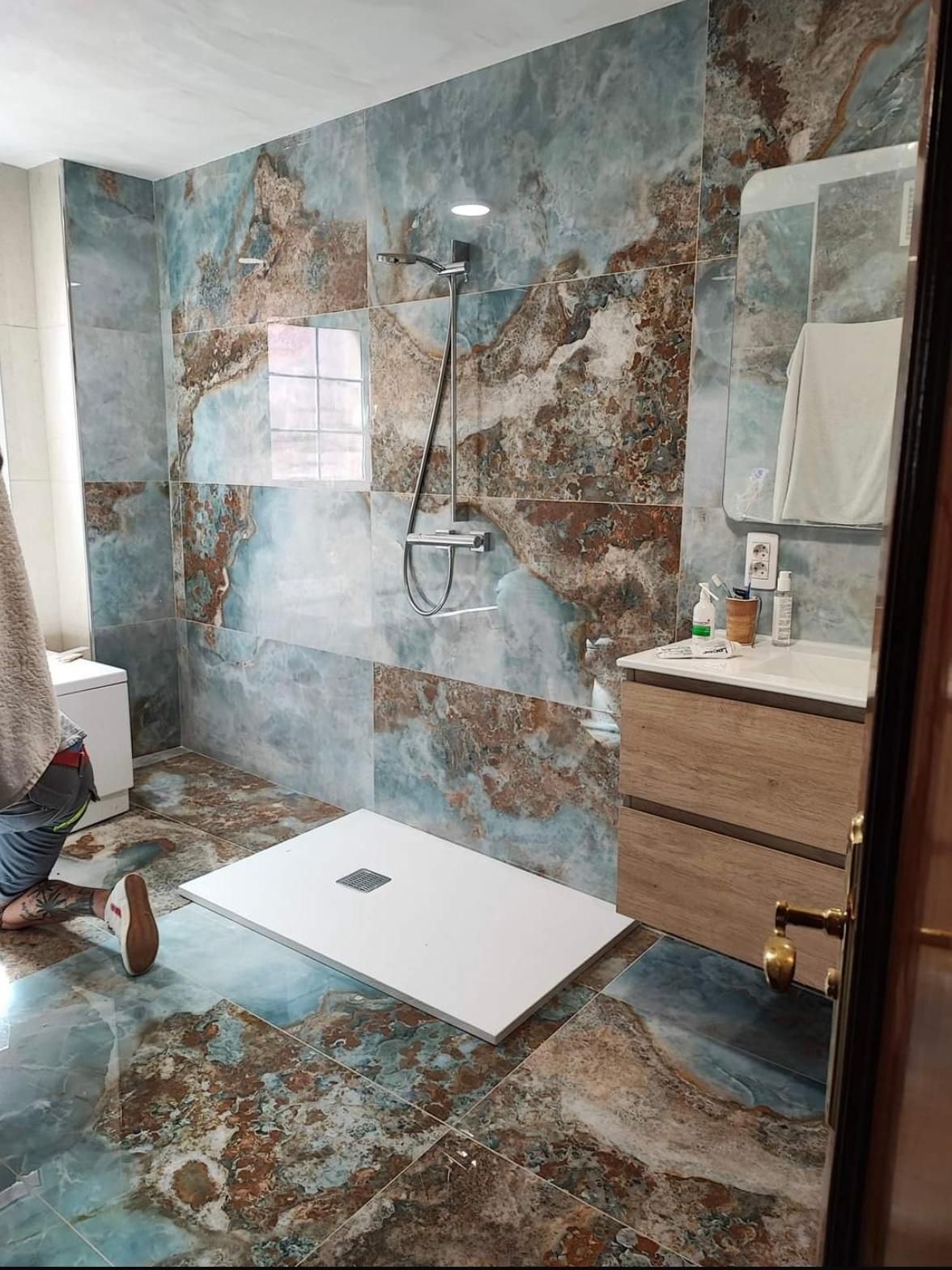 Un baño moderno con azulejos de imitación mármol azul y marrón. Incluye ducha, tocador y un aseo.