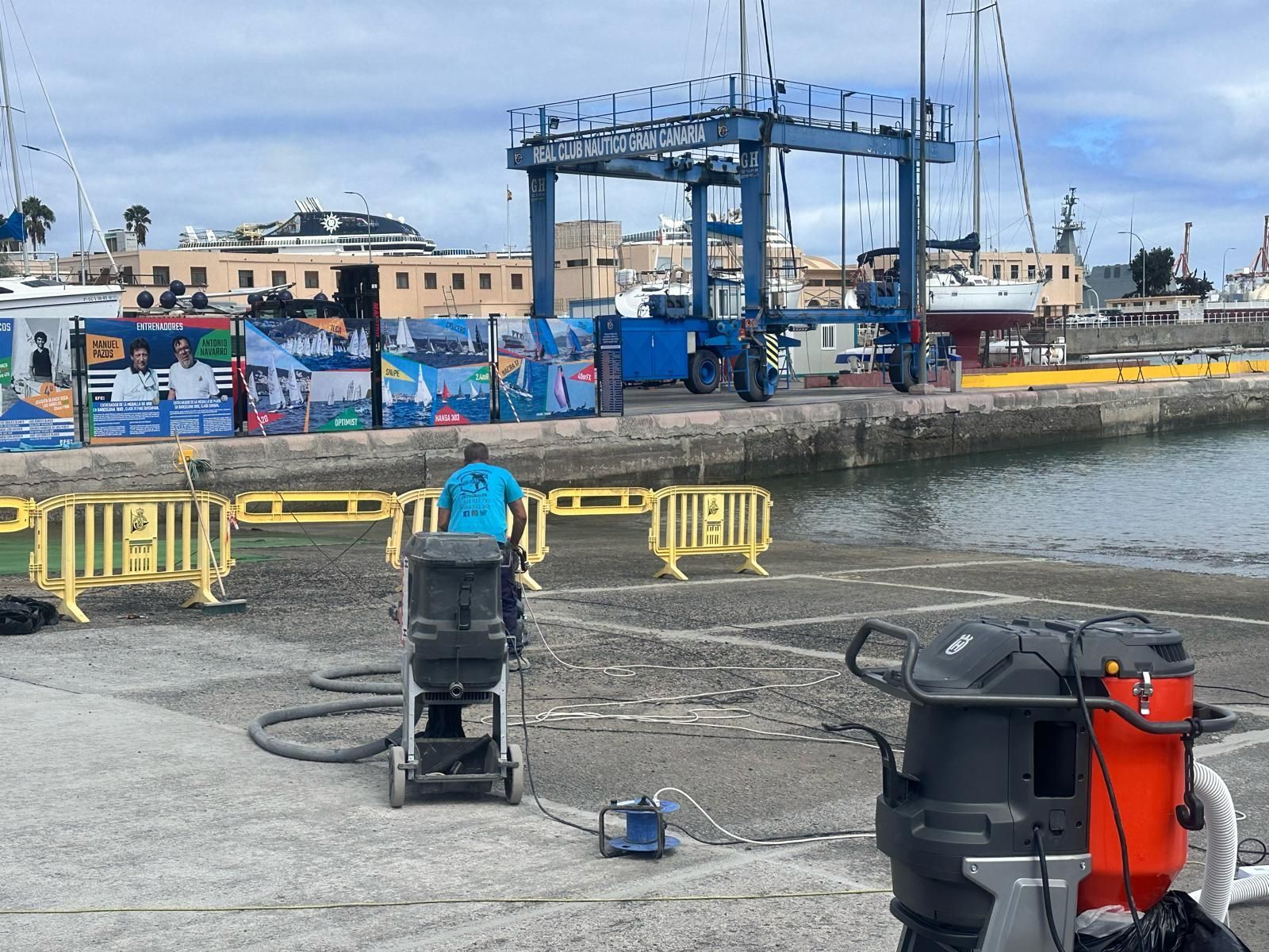 Hombre utilizando equipo industrial para limpiar un muelle junto al agua, con el puerto al fondo.
