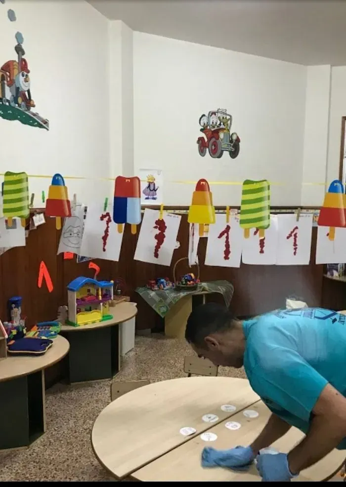 Hombre limpiando una mesa redonda en un aula decorada con adornos de temática de helados y dibujos de niños.