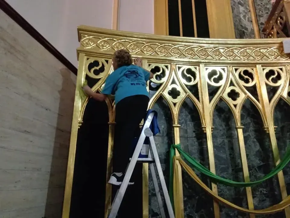 Persona en una escalera pintando un borde dorado sobre una estructura decorativa con paneles arqueados.