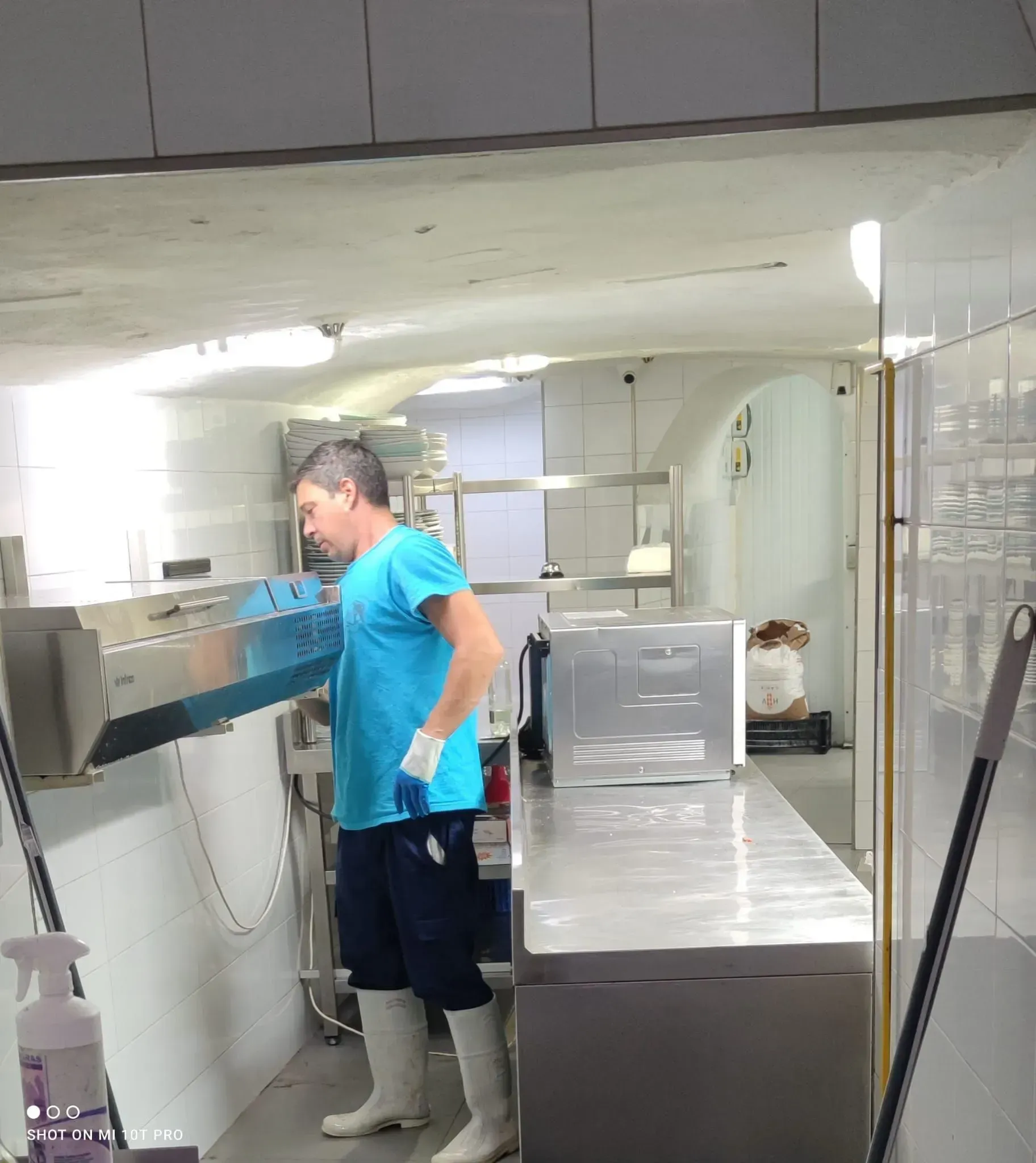 Una persona con camisa azul y botas trabaja en una cocina de acero inoxidable.