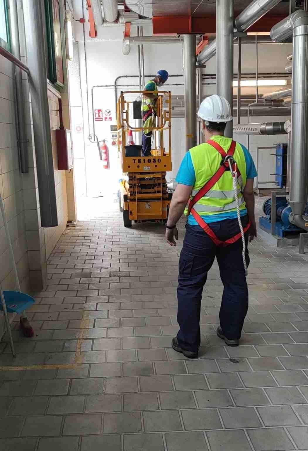 Un trabajador con chaleco de seguridad observa a otro en un elevador. Interior industrial.