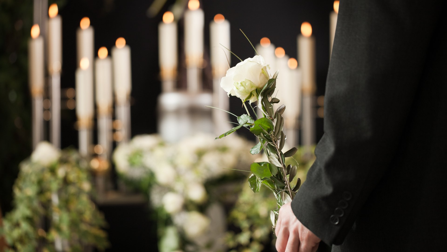 Une personne de dos pendant des funérailles avec une rose blanche dans les mains