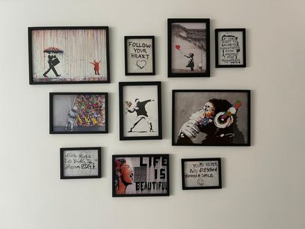 Pared de galería con pequeñas láminas y citas enmarcadas sobre una pared clara, principalmente marcos negros con piezas abstractas coloridas.