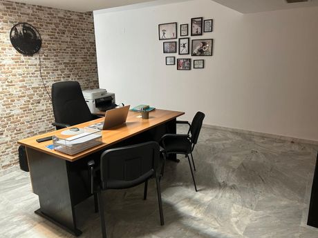 Oficina vacía con un escritorio, una computadora portátil, sillas negras, una pared decorativa de ladrillo visto y fotos enmarcadas en una pared blanca.