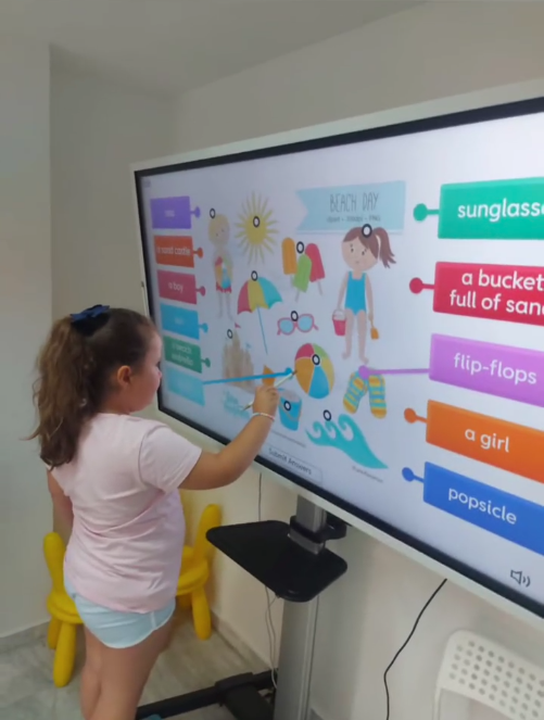 Un niño señala una colorida aplicación educativa en una gran pantalla de televisión en un entorno doméstico.