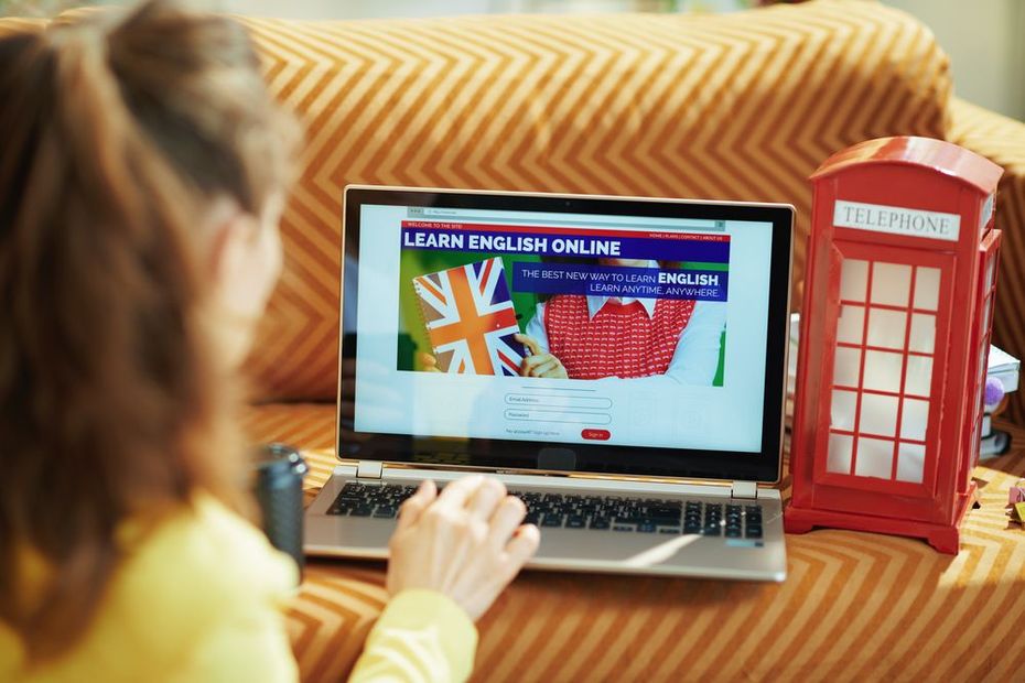 Una persona utiliza un ordenador portátil con una página web para aprender inglés, junto a una cabina telefónica roja decorada.
