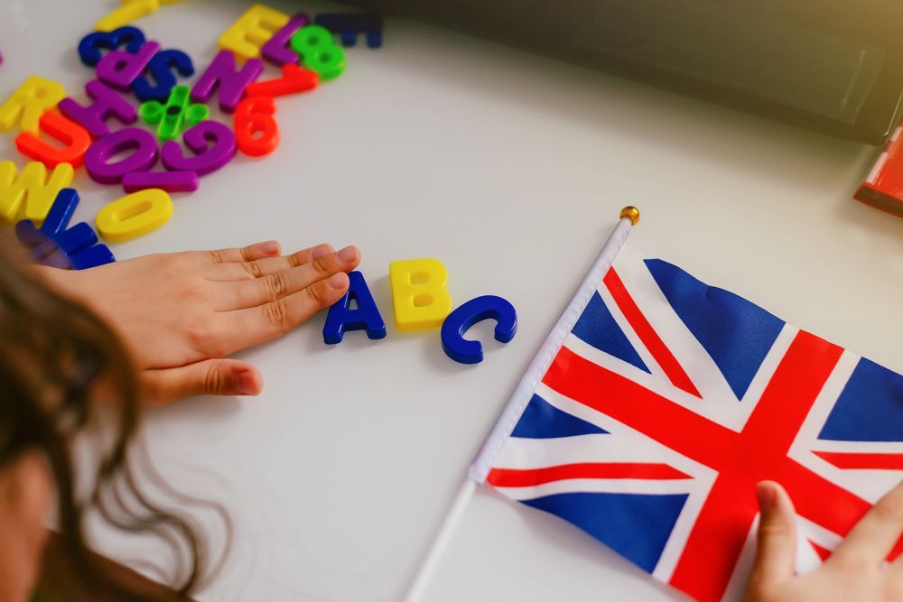 Un niño coloca letras de colores del alfabeto junto a una pequeña bandera británica sobre una mesa.