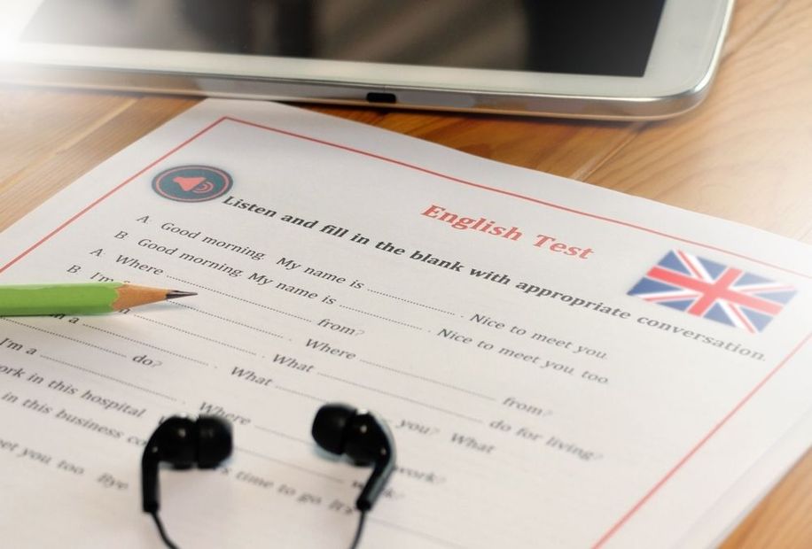 Formulario de examen de inglés sobre un escritorio con lápiz, auriculares y una tableta cerca.