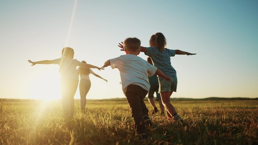 Niños corriendo con los brazos extendidos en un campo iluminado por el sol al atardecer.