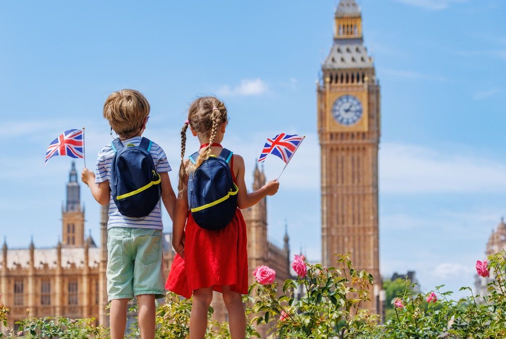 Dos niños que sostienen banderas británicas contemplan el Big Ben en Londres en un día soleado.